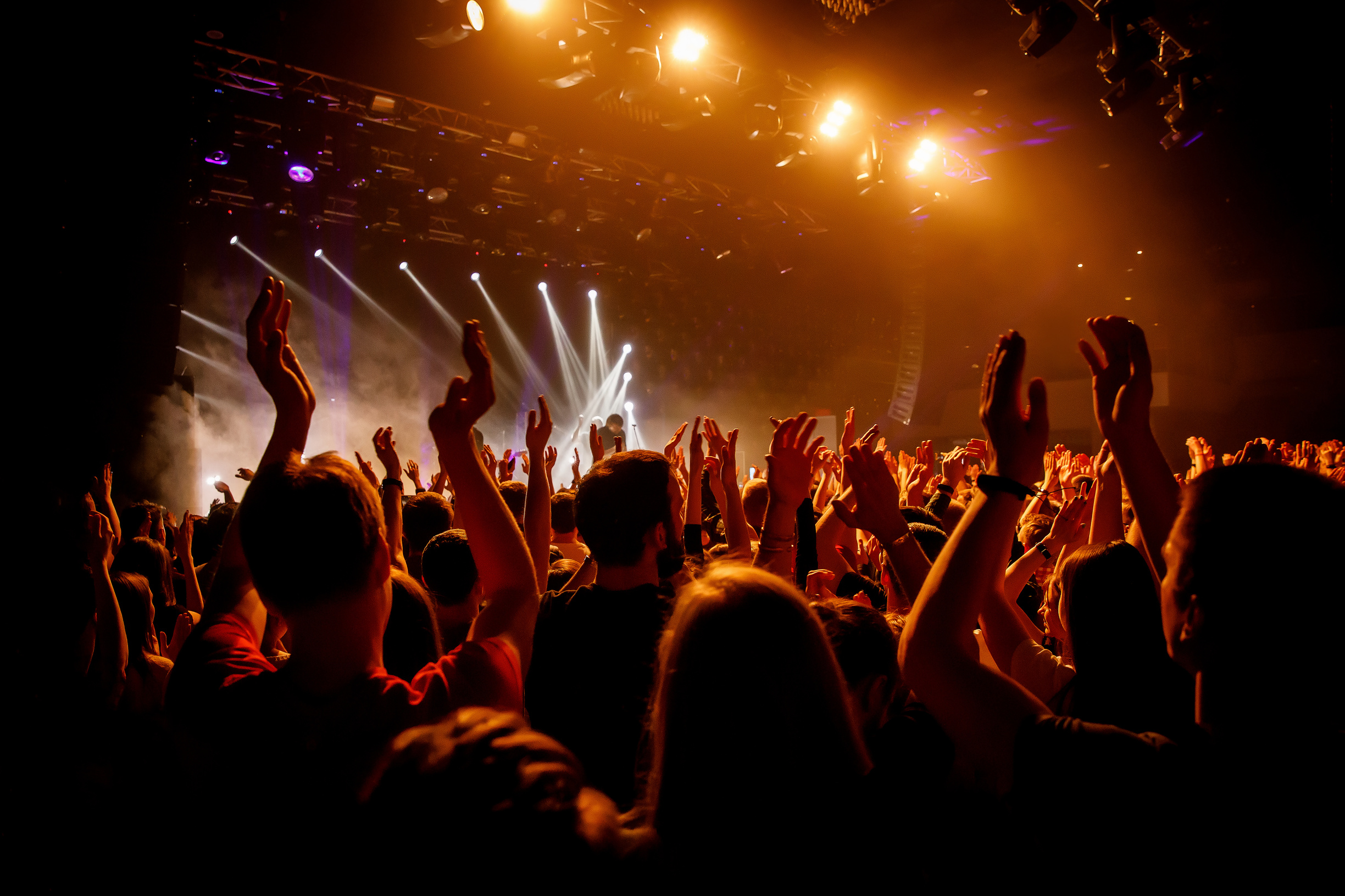 Crowd on music show, happy people with raised hands. Orange stage light.